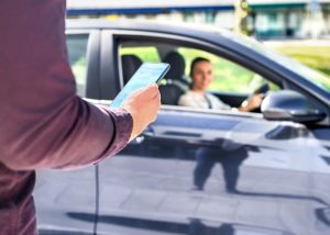 A rideshare driver in a car greeting a passenger, symbolizing the professional activity that requires special rideshare insurance coverage.