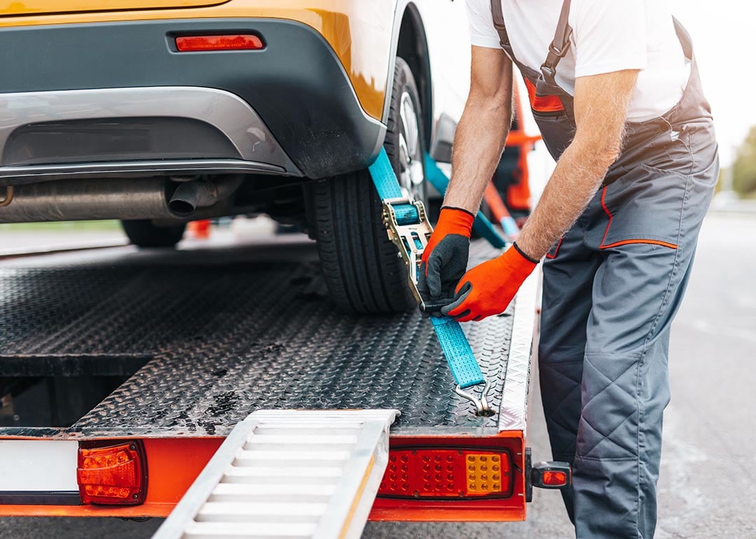 A man securing a car to a tow truck, symbolizing the process of getting a vehicle towed and the need for proper towing coverage.